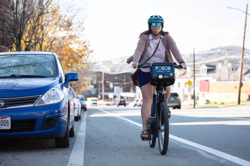 Woman wearing helmet riding POGOH bike share bike in bike lane in Pittsburgh, PA.
